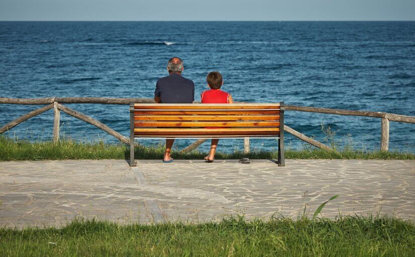 two person sitting on bench beside body of water