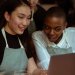 Smiling coworkers in aprons using laptop together